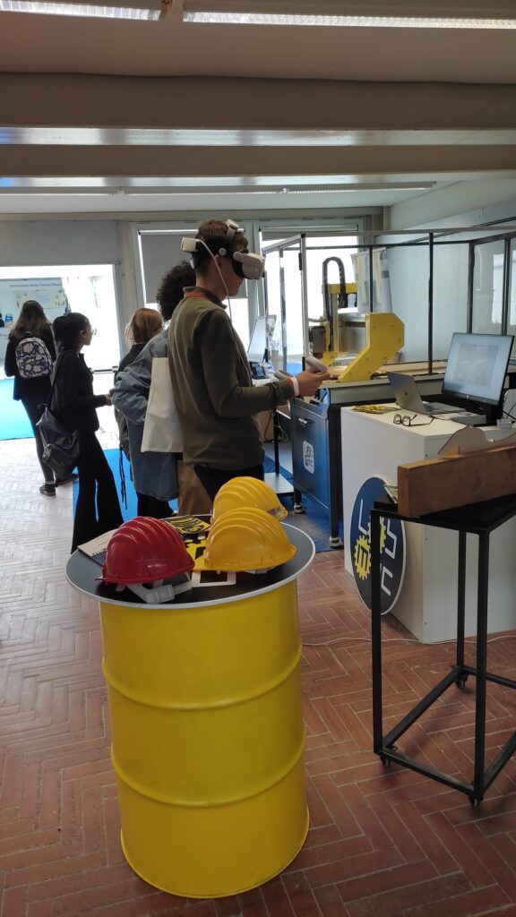 Studente prova visore VR nello stand LabMec con macchine CNC e elmetti di sicurezza Open Day scuola